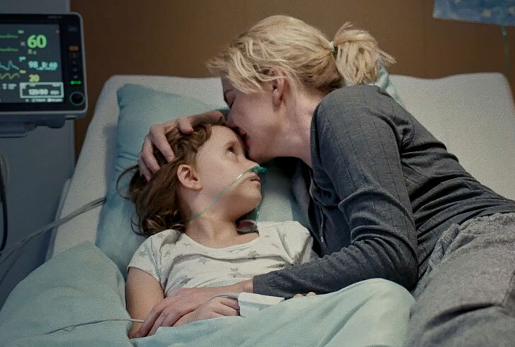 Zdjęcie dziecka na szpitalnym łóżku, obok leży matka całując je w czoło.